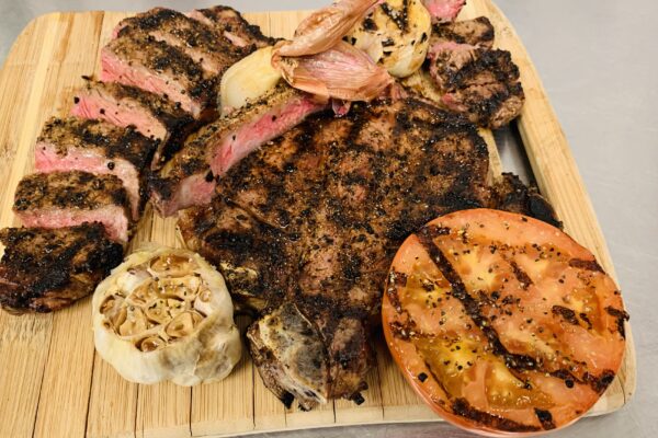 Grilled steak with roasted garlic and grilled tomato served on a wooden board.