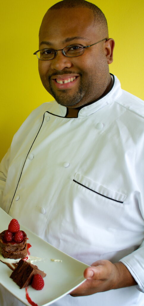 “Chef Wendell White in a white chef coat holding a plated chocolate dessert.