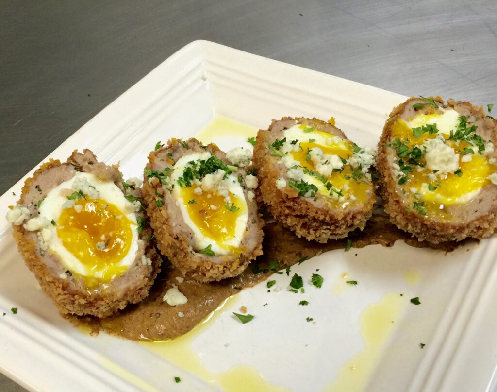 Scotch egg with spicy brown mustard sauce and shaved blue cheese on the plate