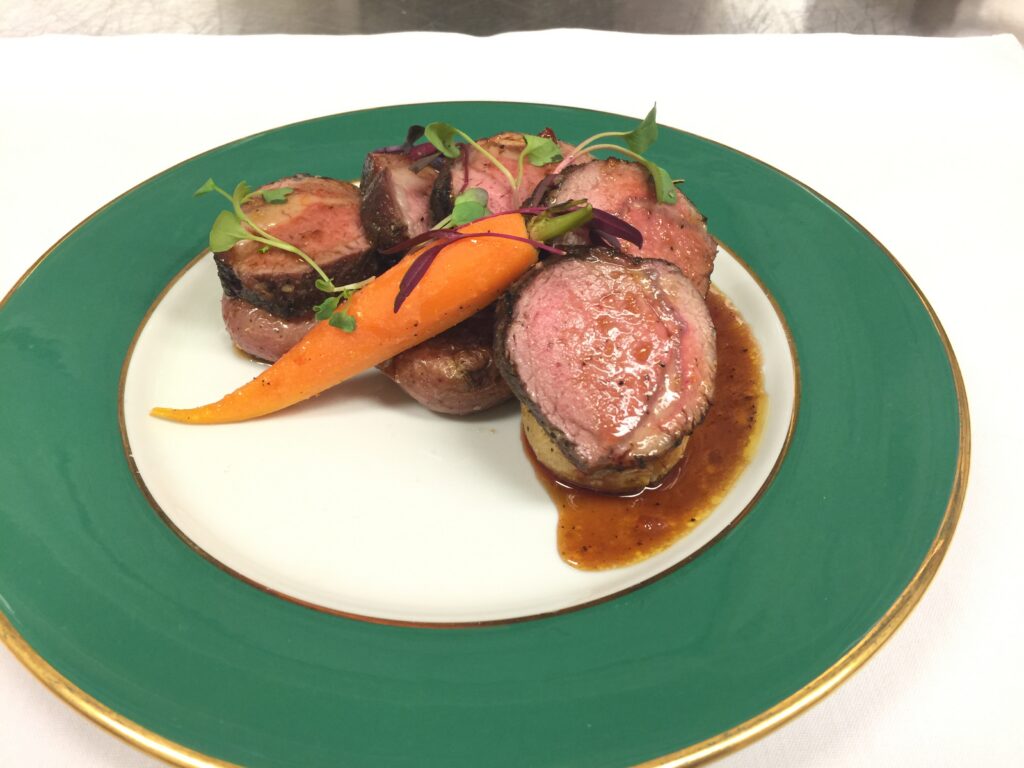 Pan roasted lamb loin plated with crispy smashed baby red potatoes, lamb jus pan sauce, and maple glazed carrot