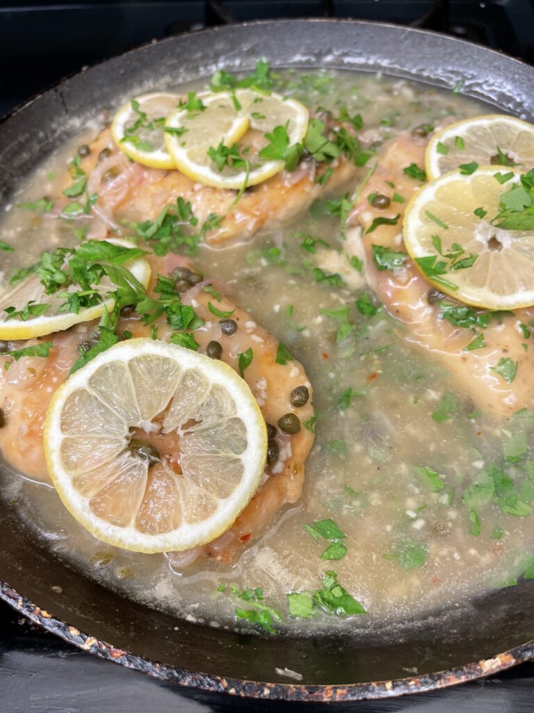 Chicken Piccata simmering in a lemon caper sauce with capers, fresh parsley, and sliced lemons.