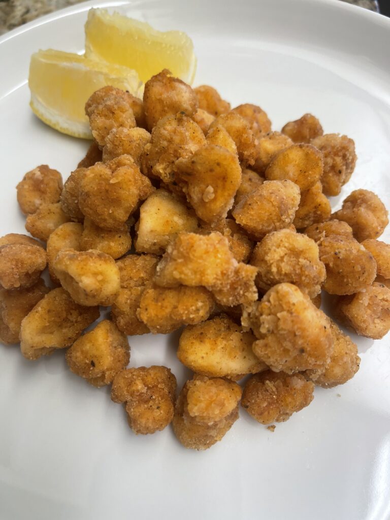 A plate of crispy golden fried bay scallops served with fresh lemon wedges on a white plate
