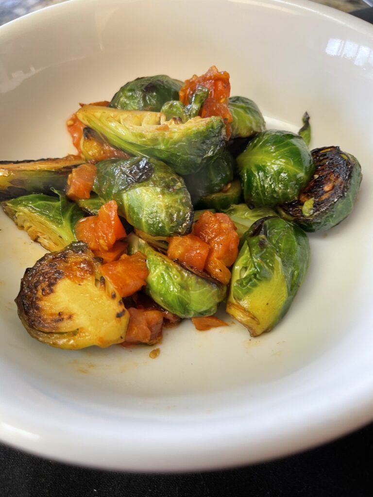 Gochujang maple Brussels sprouts with roasted red tomatoes, caramelized edges, and real organic Vermont maple syrup in a white bowl.
