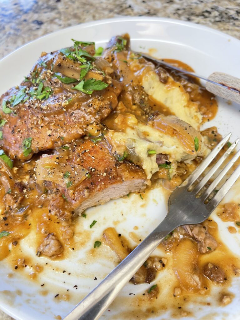 Smothered pork chops topped with rich mushroom onion gravy served over creamy mashed potatoes on a white dinner plate.
