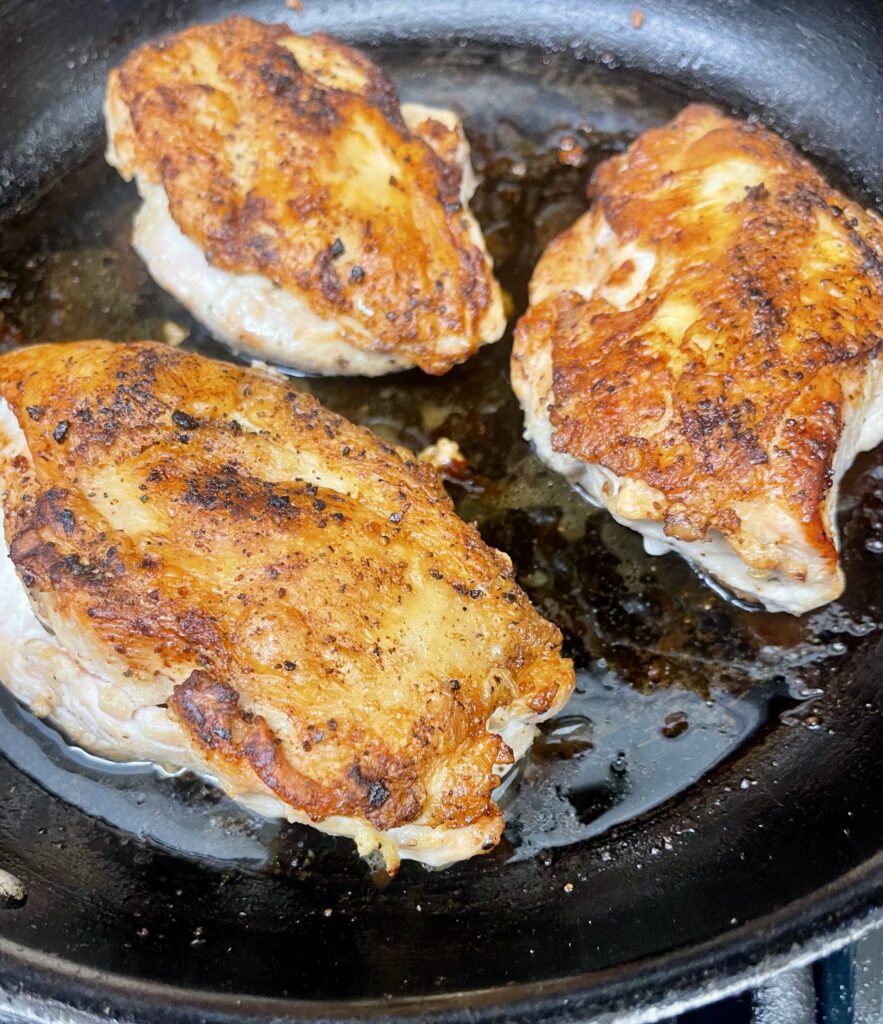 Golden-brown pan-roasted chicken breasts with crispy skin in a cast-iron skillet.