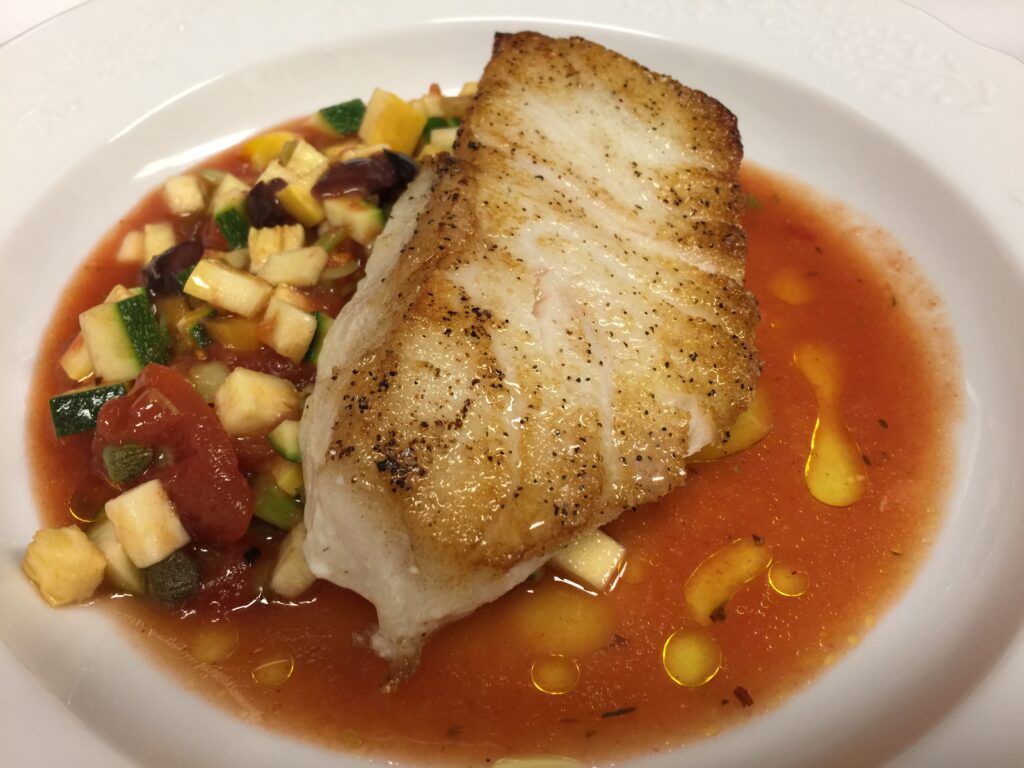 Seared Alaskan halibut served in gazpacho with fresh vegetables and olive oil.
