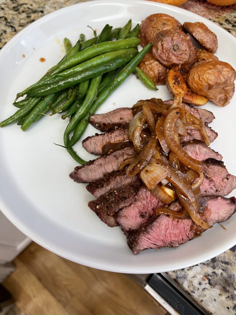 Sliced seared steak with caramelized onions, roasted potatoes and green beans demonstrating restaurant-quality cooking techniques